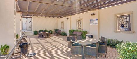 An outdoor patio area with a covered seating arrangement, a table, and chairs.