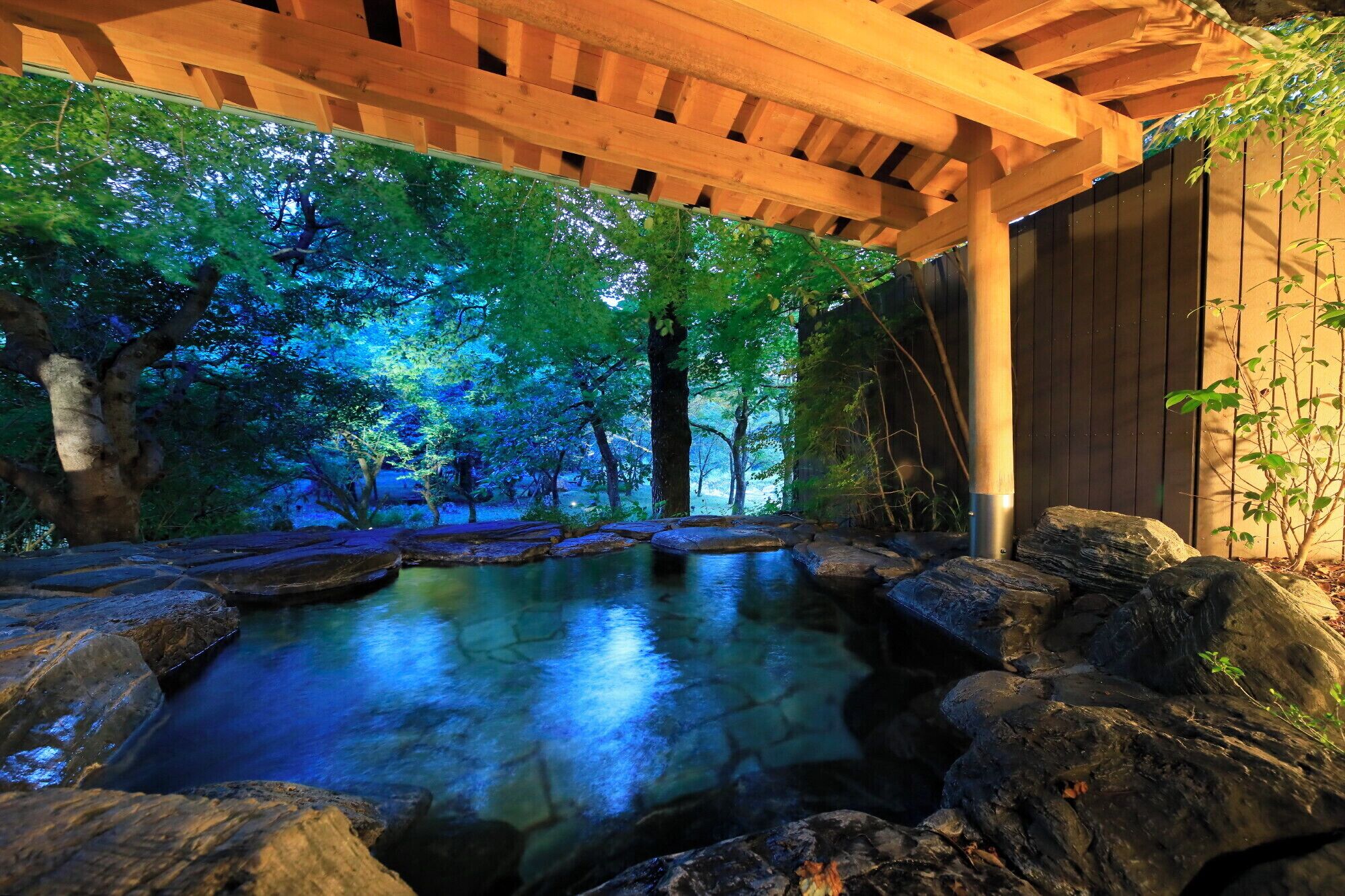 Un jardín interior tranquilo con fuente de agua, pérgola de madera y pared de madera.