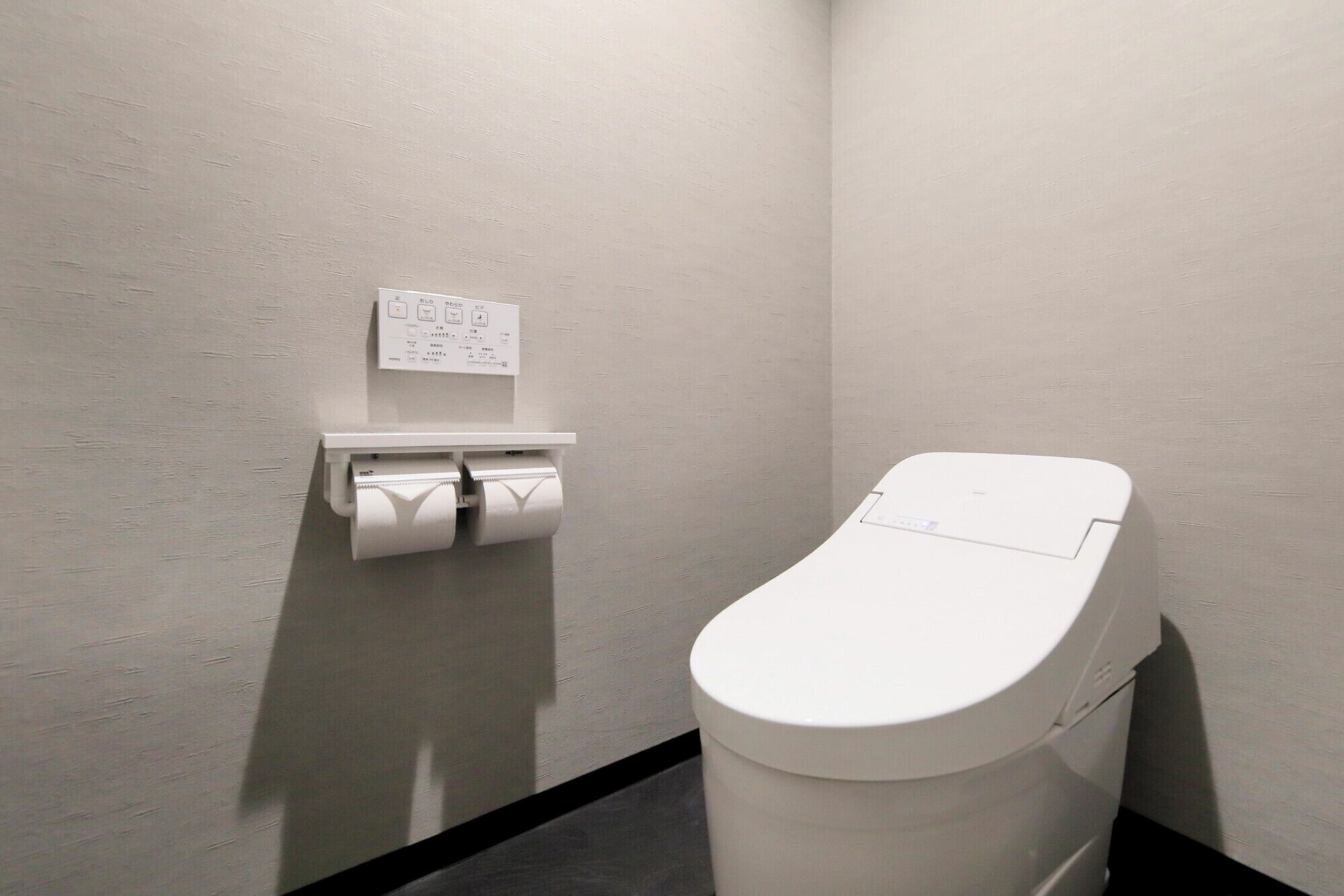 Un bagno moderno e piccolo, con il water, un dispenser di carta e una presa elettrica a muro.
