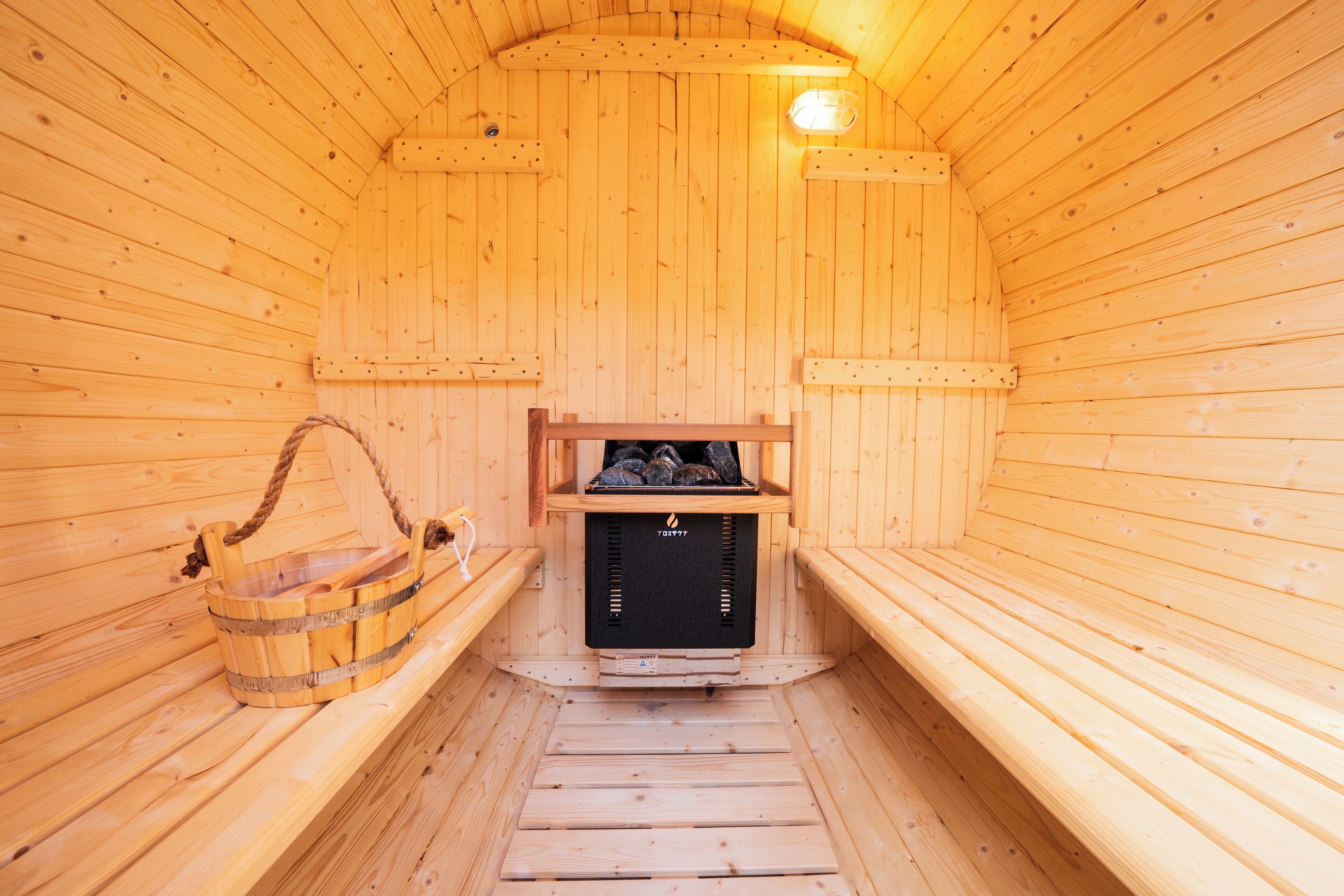 Una sauna de madera con bancos, un banco con una toalla y un cubo de madera.