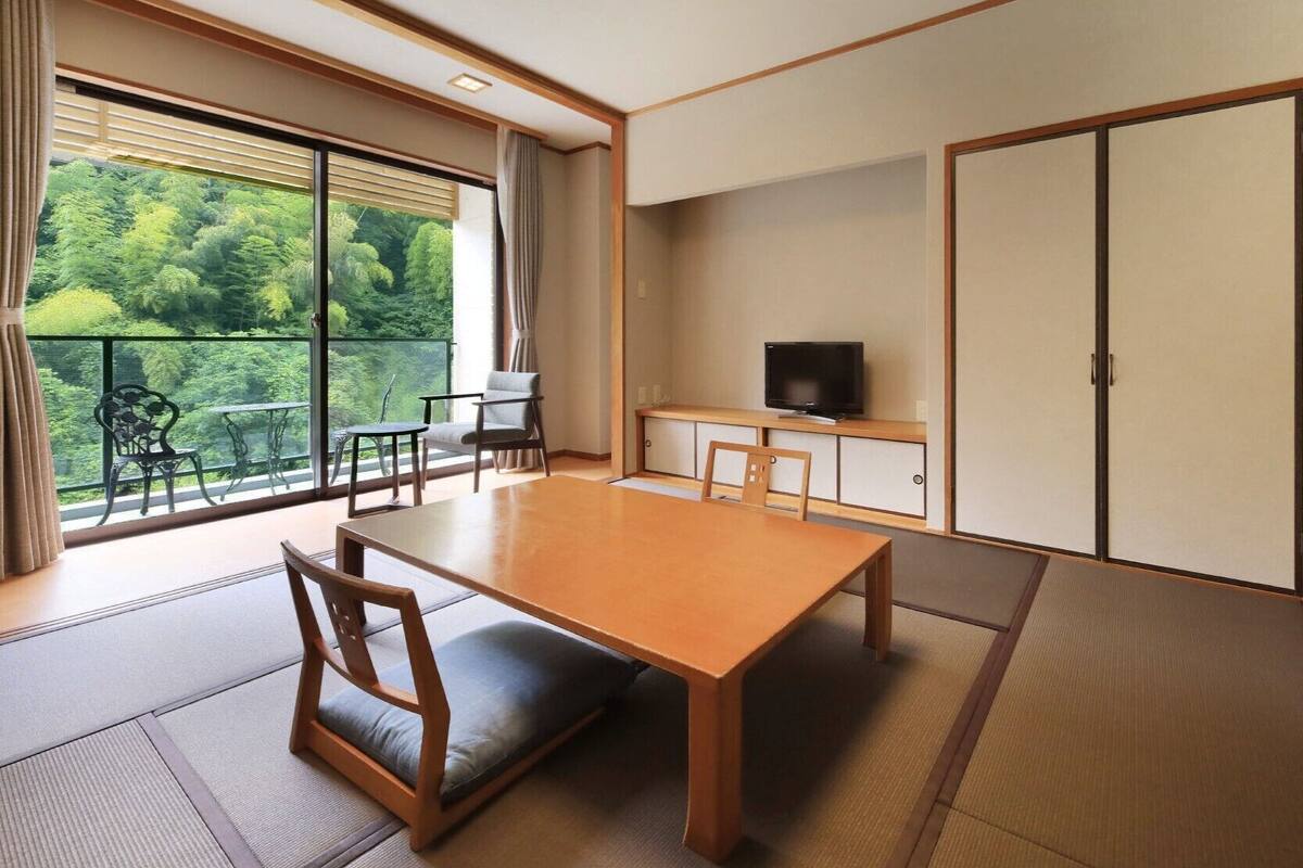 A traditional Japanese-style room with tatami flooring, a low table, and a television on a shelf.