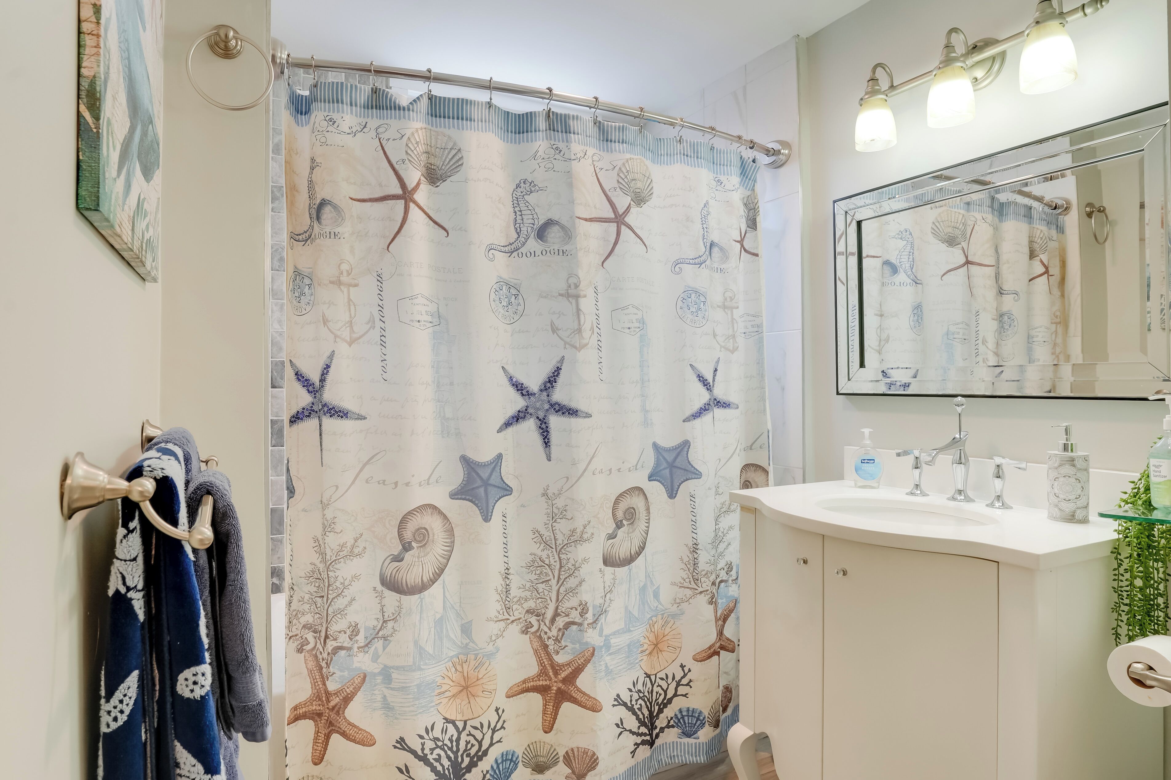 Un baño con cortina de ducha con motivos marinos, un lavabo con artículos de aseo y un espejo encima.