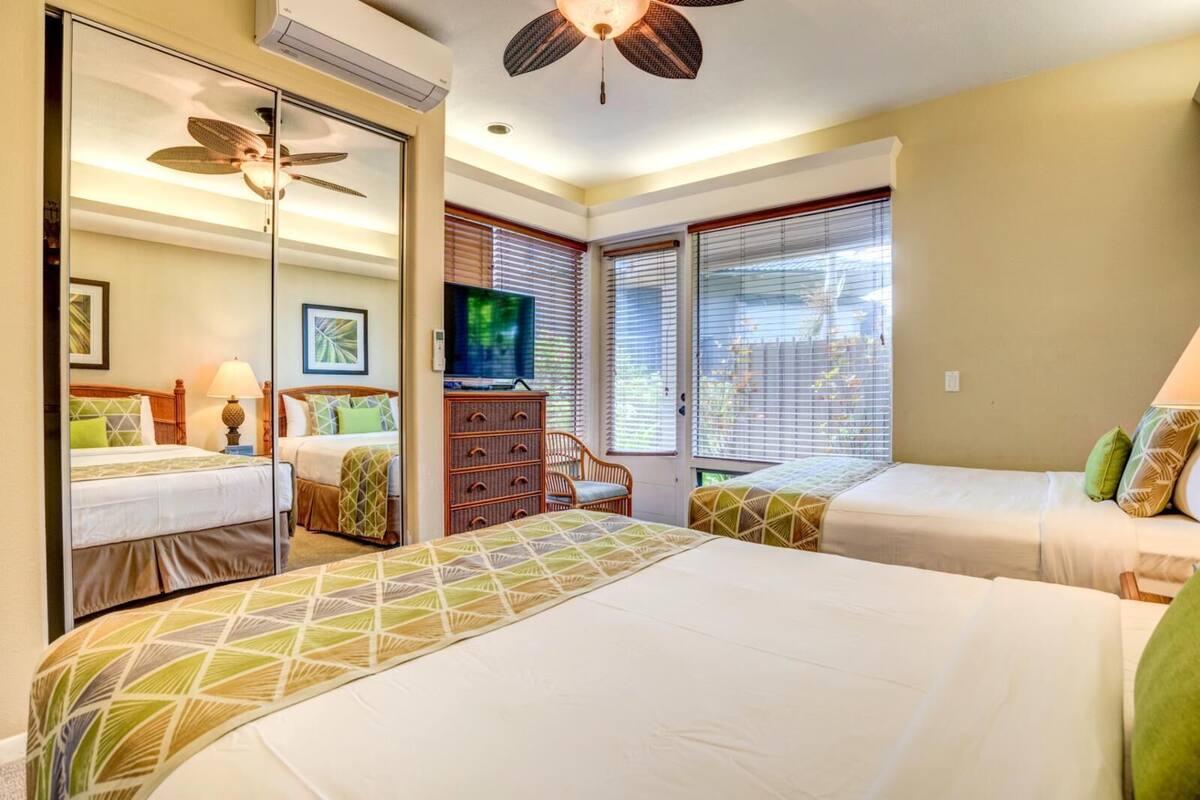 Quarto de hotel com duas camas, televisão, ventoinha no teto e janela com persianas.