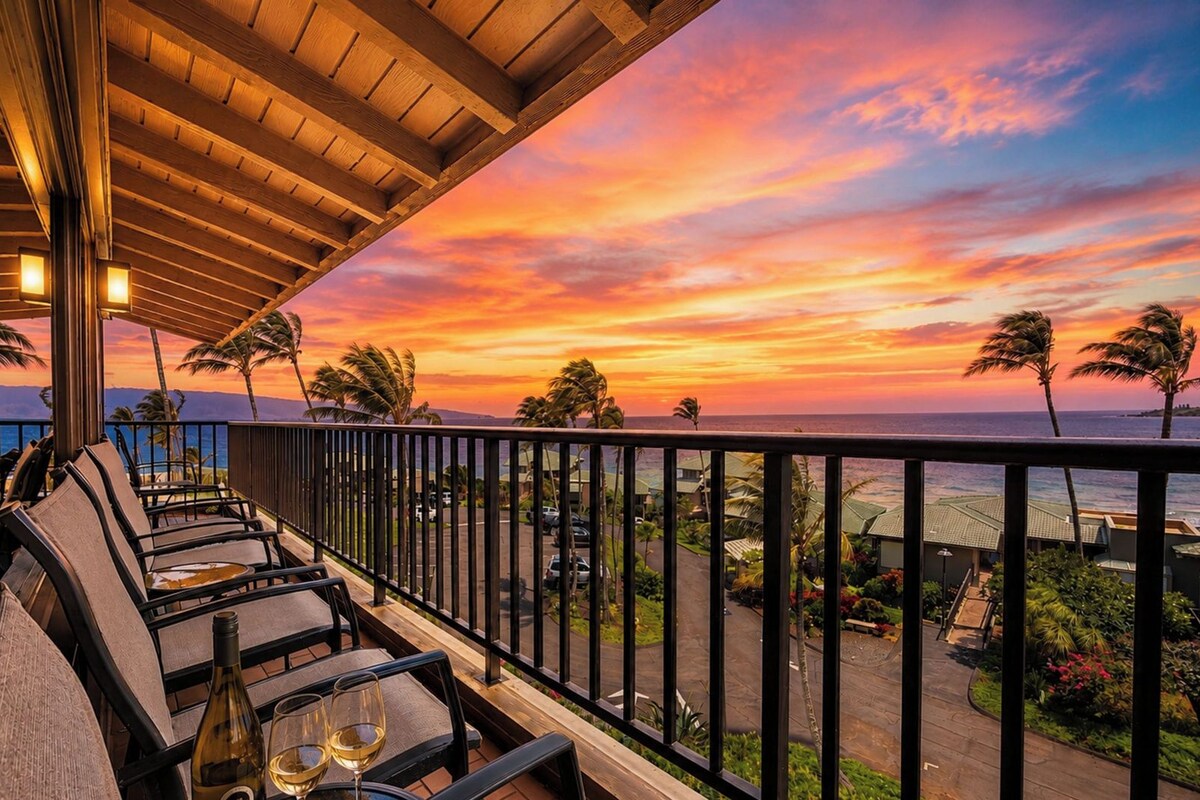 A terrace with outdoor seating and a view of the ocean at sunset.