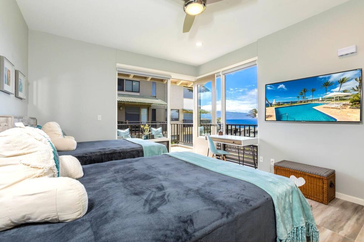 Quarto de hotel com duas camas, varanda com vista para o mar e área de refeições com mesa e cadeiras.