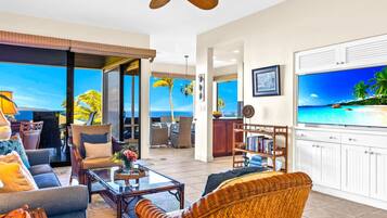 A spacious living room with a large TV, comfortable seating, and a view of the ocean.