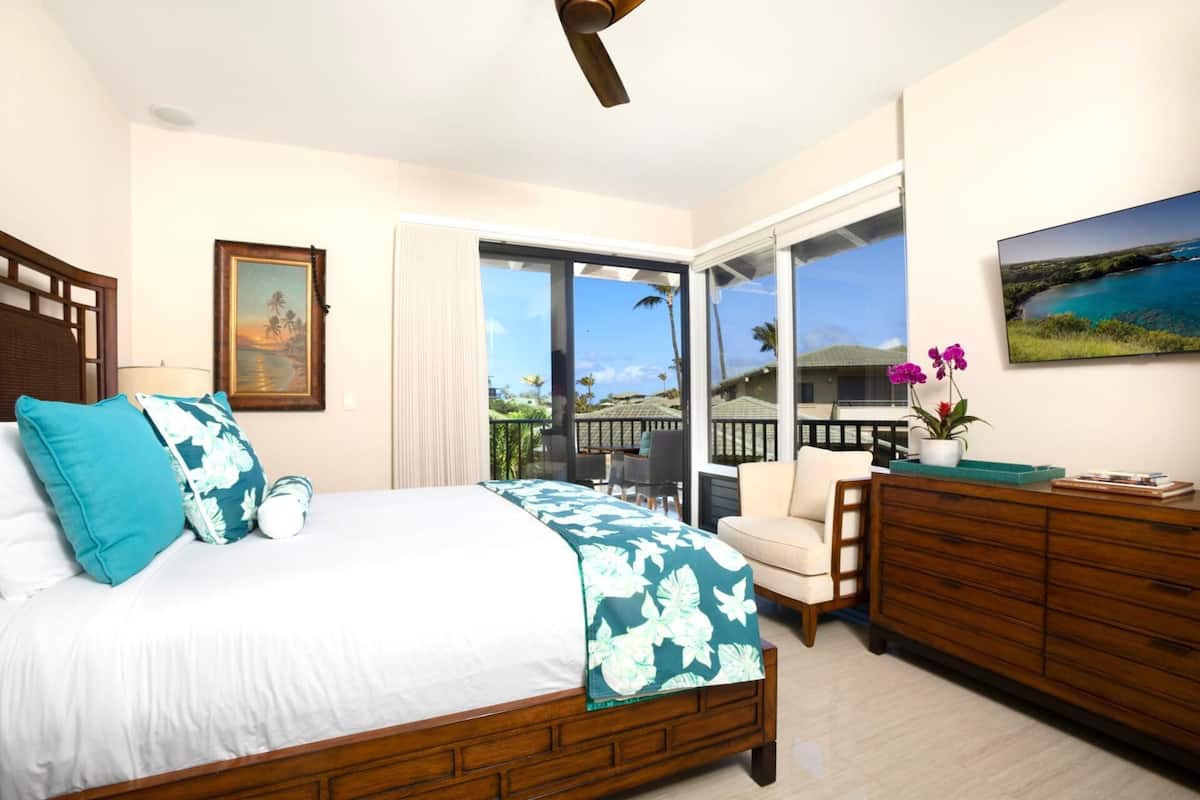 Quarto com cama, cômoda, cadeira, um quadro e vista para o exterior.