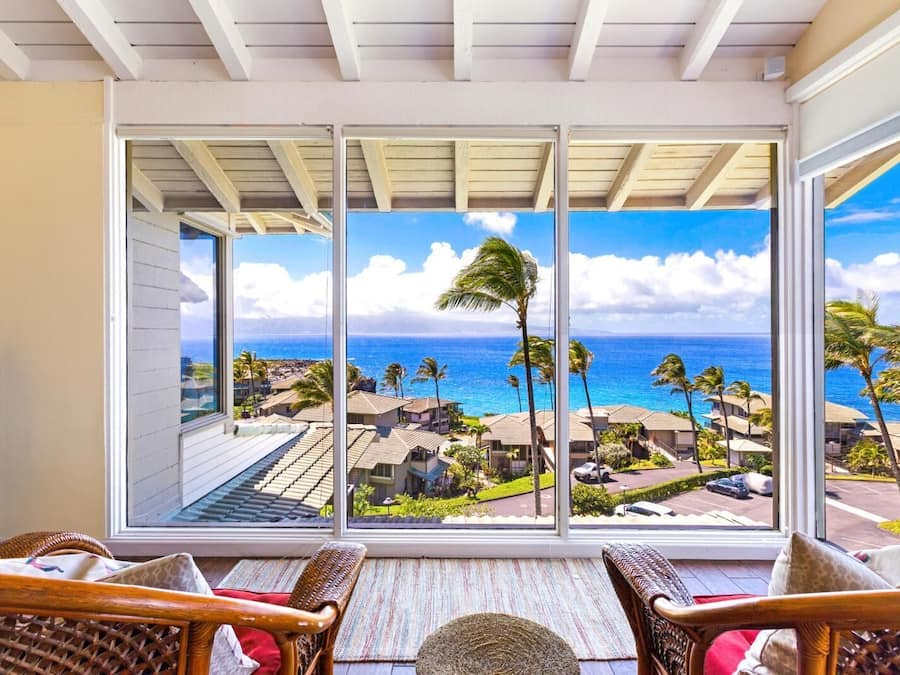 Una habitación con un amplio ventanal que da a un balcón con vistas al océano y palmeras.