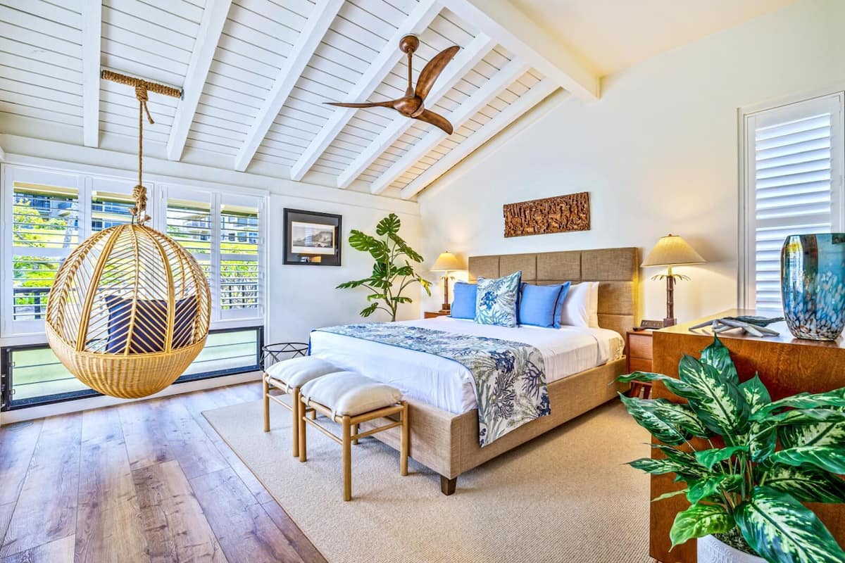 Quarto amplo com uma cama grande, uma cadeira suspensa, ventilador de teto e vista para o exterior através de janelas amplas.