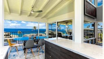 A modern kitchen with a large island, a dining area with a view of the ocean, and a ceiling fan.