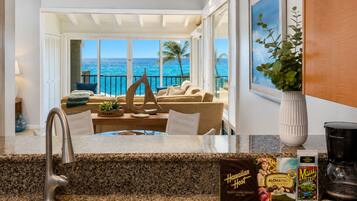 A kitchen with a view of the ocean, a dining area with a sofa and table, and a coffee station with branded items.