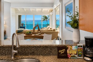 A kitchen with a view of the ocean, a dining area with a sofa and table, and a coffee station with branded items.