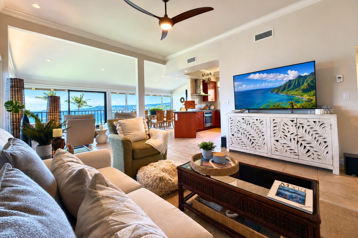A spacious living area with a large sofa, a coffee table, and a television mounted on a white cabinet with intricate leaf patterns.