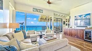 A spacious living area with a large window overlooking the ocean, a ceiling fan, and a wooden floor. - Kapalua Bay Villas Resort by KBM (Kapalua)