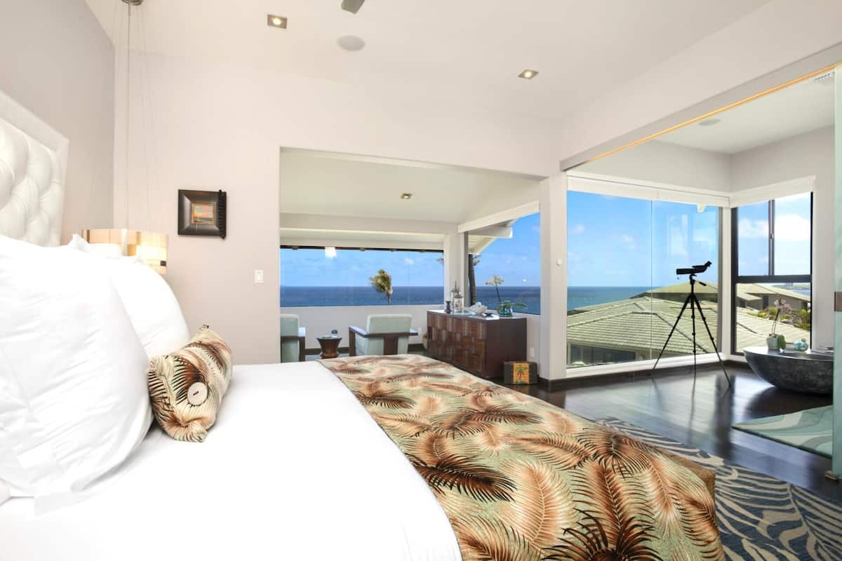 Quarto de hotel moderno com uma cama grande, vista para o oceano e um telescópio numa varanda.