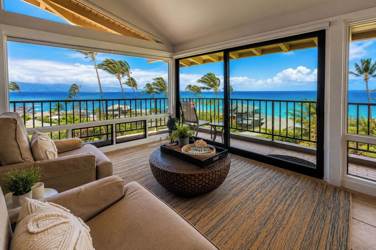 A balcony with a view of the ocean and palm trees, furnished with a sofa and a coffee table.