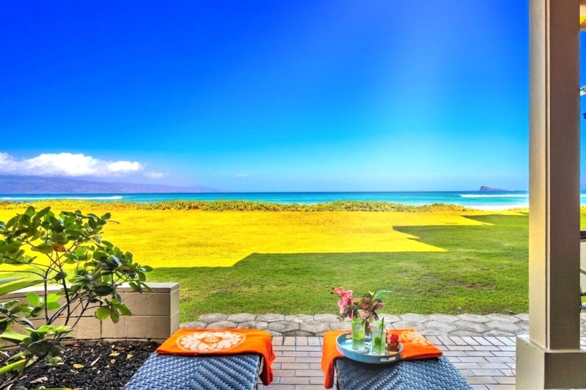 Um pátio com duas mesas de massagem, um tabuleiro com bebidas e vista para a praia e o oceano.