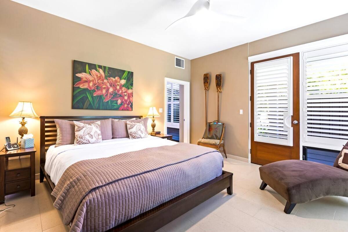 Quarto com uma cama grande, duas mesas de cabeceira com luminárias, uma cadeira, um quadro na parede e uma porta com persianas.