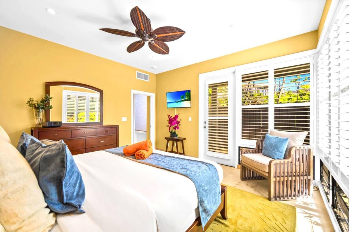 Quarto com cama, penteadeira, televisão, cadeira e varanda com persianas.