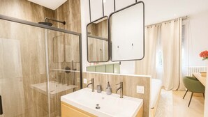Un baño moderno con cabina de ducha de vidrio, un espejo grande y un mueble de tocador con lavabo.