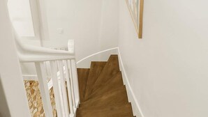 Una escalera blanca con escalones de madera y barandilla blanca, que lleva a un rellano con un cuadro en la pared.