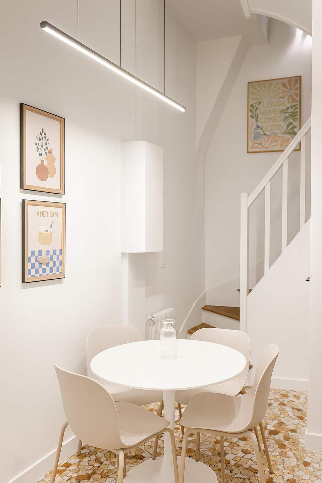 A modern dining area with a round table and four chairs, a pendant light, and framed artwork on the walls.