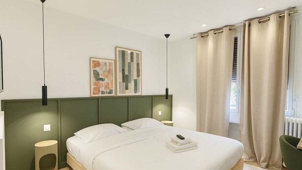 Un dormitorio moderno con una cama grande, dos mesitas de noche, una lámpara de pie y una obra de arte en la pared.