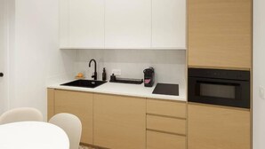 Una cocina compacta con un lavamanos negro, una cafetera y un horno empotrado.
