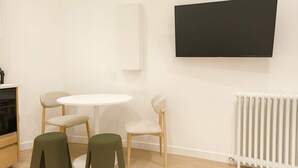 Ein modernes Zimmer mit einem runden weißen Tisch, zwei Stühlen, einer Heizung und einem an der Wand befestigten Fernseher.