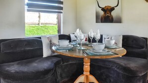 A dining area with a round wooden table, black velvet sofas, and a window with blinds.