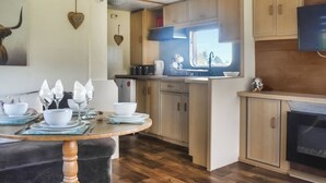 A compact kitchen with wooden cabinets, a dining table set with white dishes, and a window providing natural light.