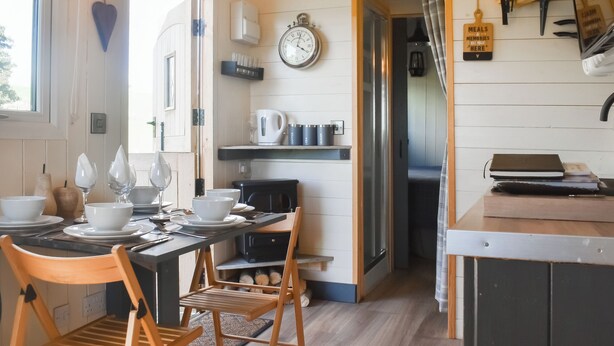 Uma cozinha acolhedora com mobiliário de madeira, uma mesa de jantar posta para quatro pessoas e um relógio na parede.