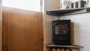 Um quarto aconchegante com uma lareira a lenha, prateleiras de madeira com canecas e uma porta.