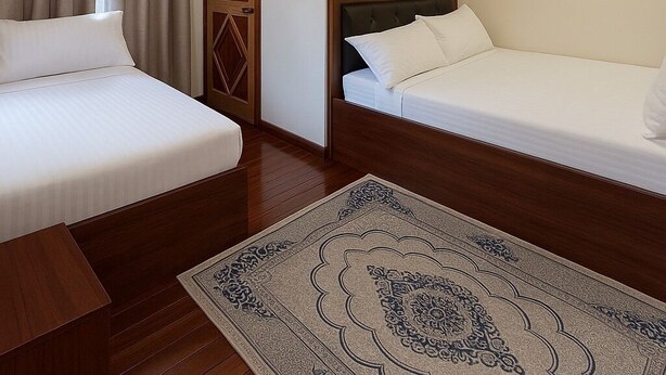 Ein Hotelzimmer mit zwei Betten, einem Holz-Kopfteil, einem gemusterten Teppich und einer Tür mit geometrischem Dekor.