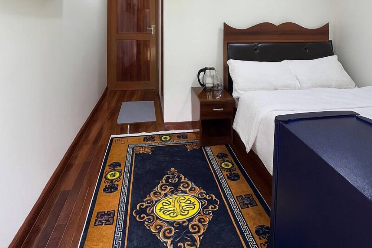 A hotel room with a bed, a nightstand, a television mounted on the wall, and a wooden door.