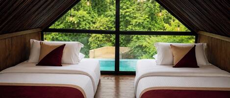 A room with two beds, wooden flooring, and a large window overlooking a green landscape.