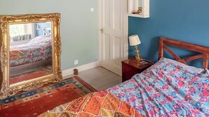 Una camera da letto con un grande specchio decorato, un letto con copriletto floreale, un comodino con lampada e una porta con specchio sopra.