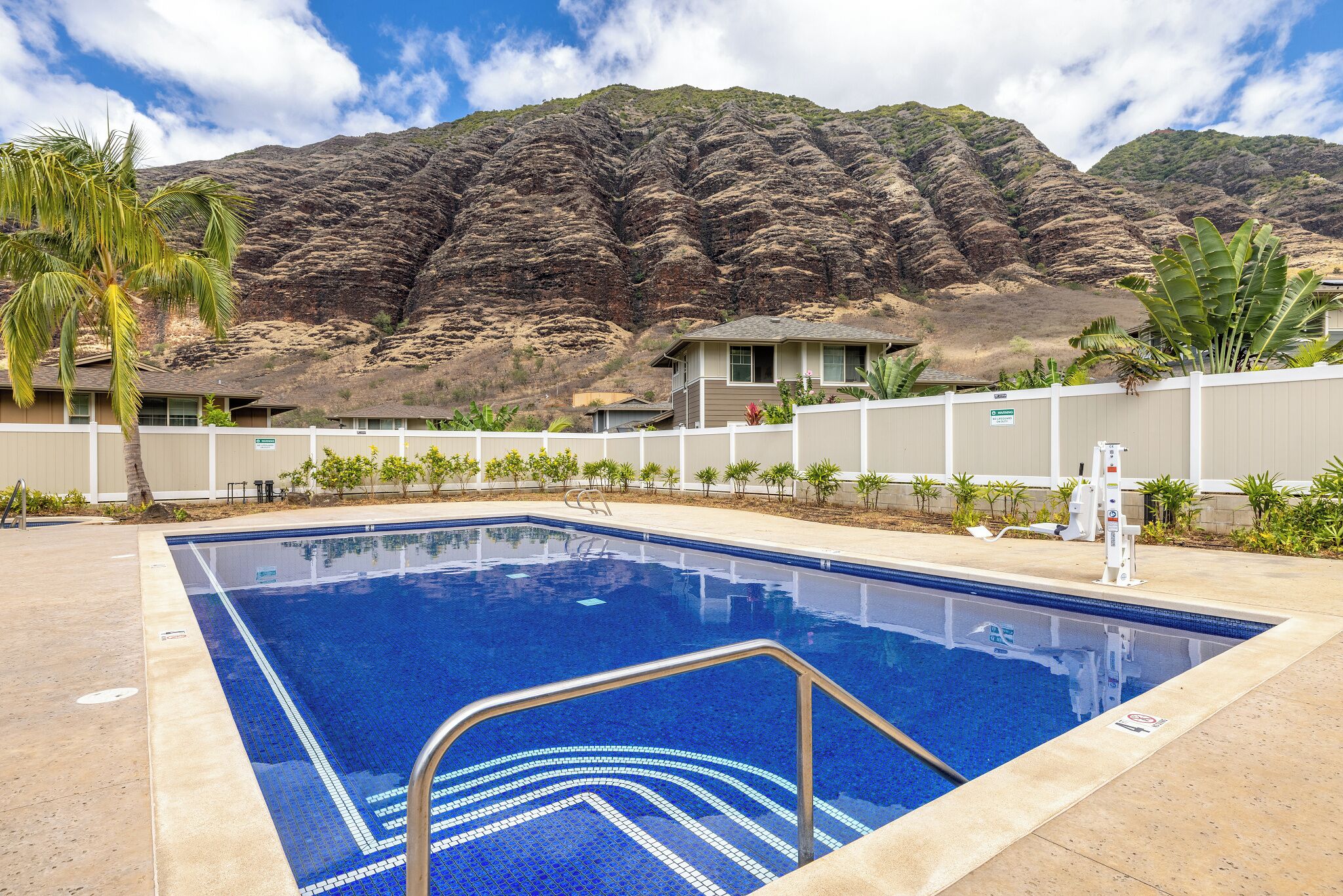 A swimming pool with a mountain backdrop, surrounded by a fence and small plants.
