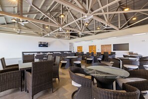 Un vaste espace intérieur doté de hauts plafonds, de plusieurs types d’aménagements pour s’asseoir, notamment des tables rondes et des chaises en osier, ainsi que de ventilateurs de plafond.