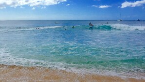 A beach with clear turquoise water, people surfing, and boats in the distance. - Studio- Ocean View Hideaway (Waianae)