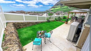 A backyard with a patio table and chairs, a grill, and a view of a residential area with houses and a hill. - Studio- Ocean View Hideaway (Waianae)
