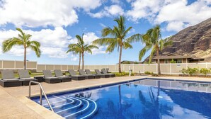 A swimming pool with lounge chairs and palm trees, surrounded by a fence and a building. - Studio- Ocean View Hideaway (Waianae)