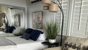 A modern bedroom with a large bed, a sofa, a coffee table, a potted plant, and a painting on the wall. - Studio- Ocean View Hideaway (Waianae)