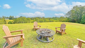 Ein grüner Außenbereich mit einem runden Metalltisch und vier Holz-Adirondack-Stühlen.