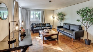 A modern living room with a sectional sofa, a coffee table, and two potted plants. - Fish, Hike, Golf! Accessible Baldwin Home w/ Yard (Baldwin)