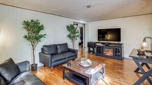 A modern living room with a sofa, coffee table, and TV. - Fish, Hike, Golf! Accessible Baldwin Home w/ Yard (Baldwin)