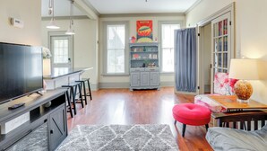A spacious living room with a flat-screen TV, a red ottoman, a wooden coffee table, and a chandelier. - Franklin Home w/ Deck, Creek Views: Walk to Shops (Franklin)