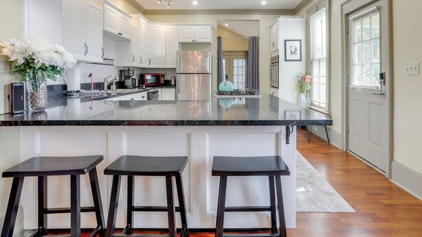 A modern kitchen with white cabinets, a black marble countertop, and three black stools. - Franklin Home w/ Deck, Creek Views: Walk to Shops (Franklin)