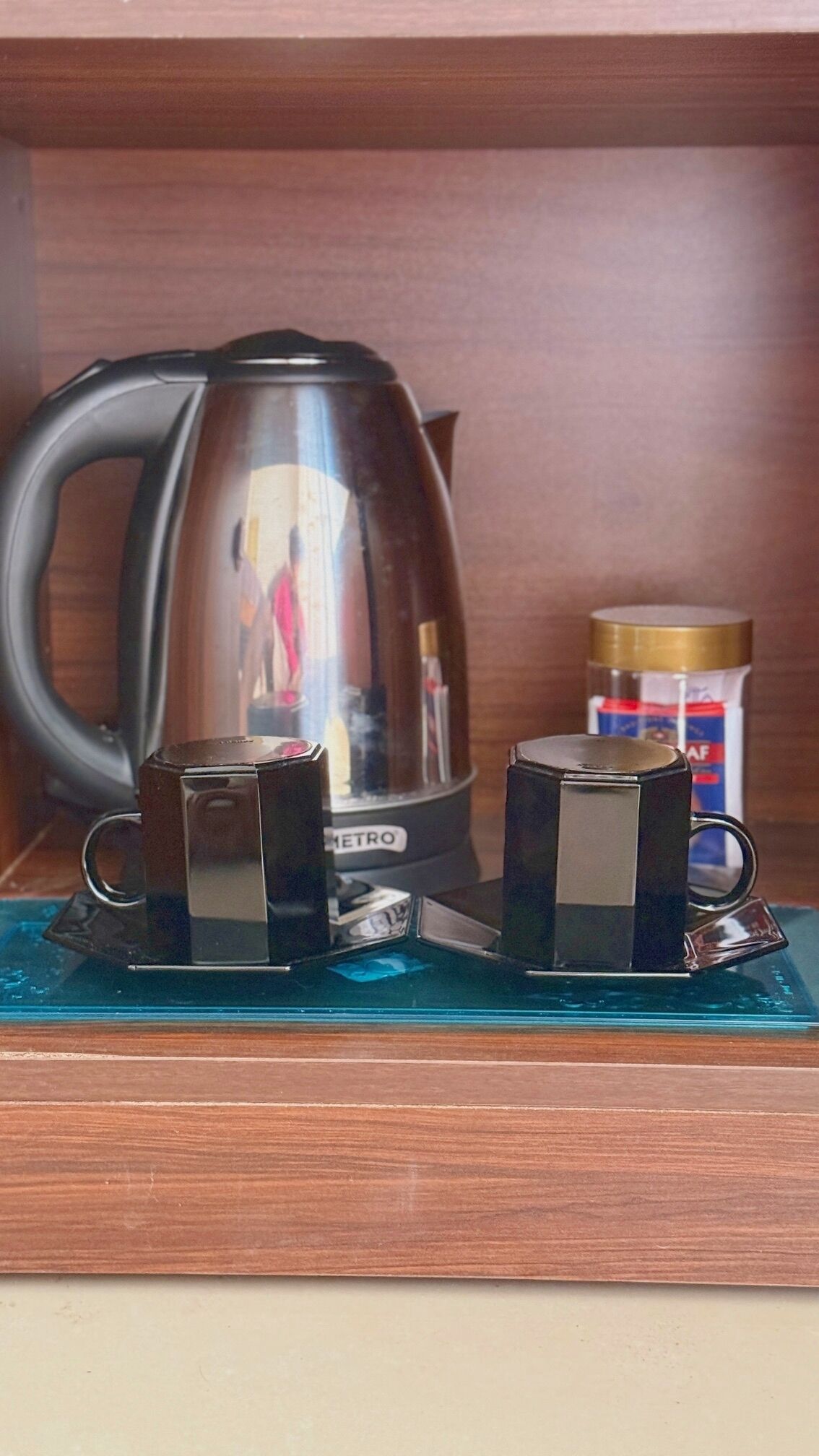 A coffee maker, two cups, and a container on a wooden shelf.
