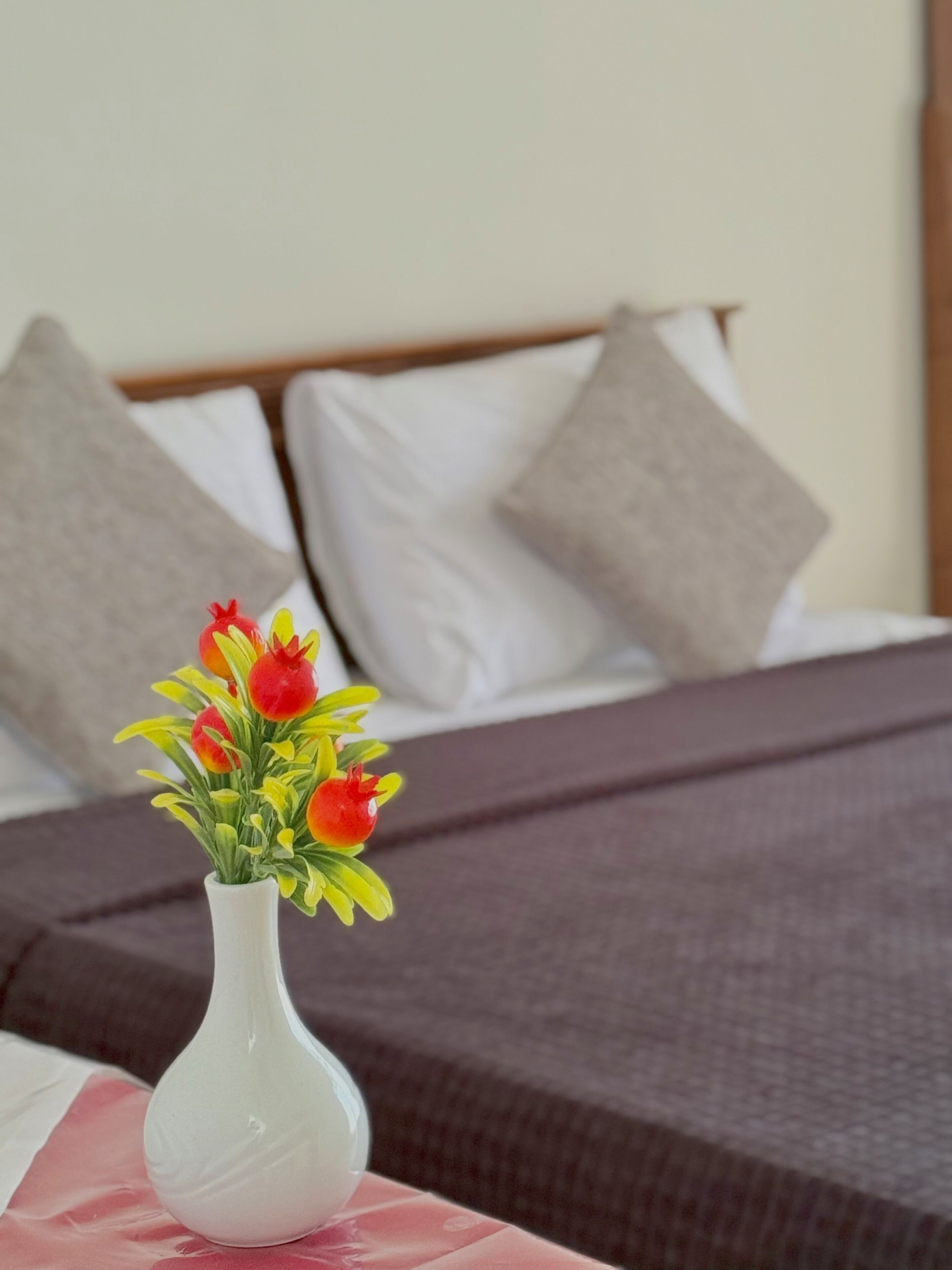 A white vase with a bouquet of red and yellow flowers on a table in a hotel room.